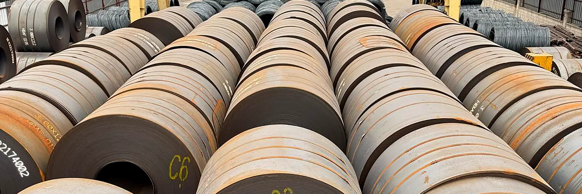 Rows of hot-rolled steel coils under a yellow gantry crane