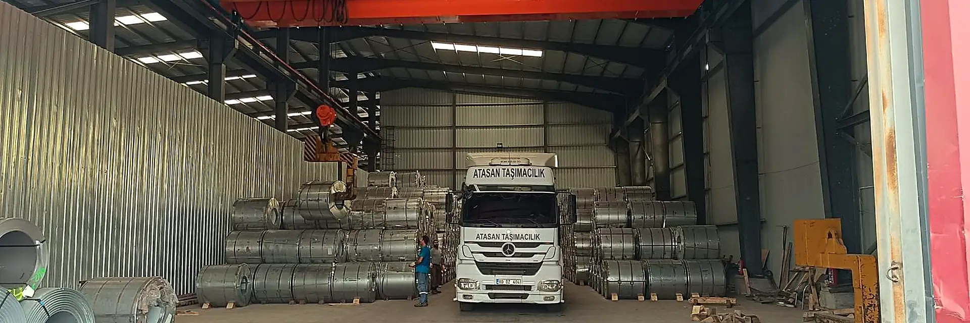 Warehouse interior with a lorry pulled in for loading and a red overhead crane